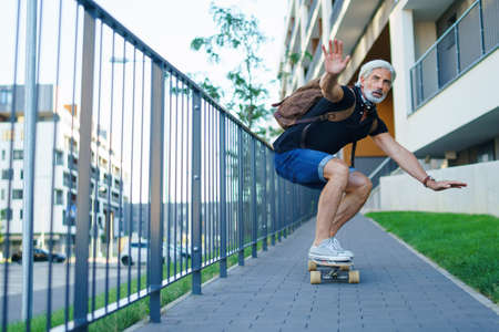 Portrait of mature man riding skateboard outdoors in city, going back to work.の写真素材