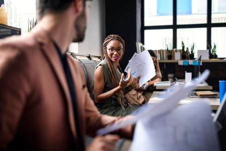 Portrait of young business people with laptop working indoors in office, talking.の写真素材