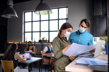 Business people with face masks indoors in office, back to work after coronavirus lockdown.の写真素材