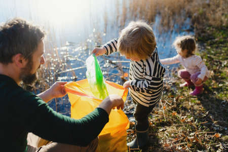 Father with small kids collecting rubbish outdoors in nature, plogging concept.の写真素材