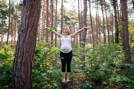 Portrait of happy barefoot pregnant woman outdoors in nature, doing exercise.