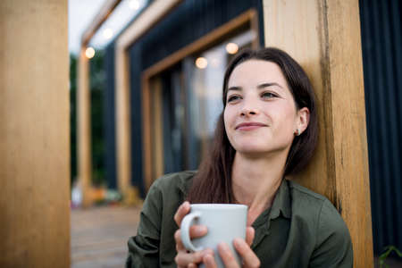 Young woman with coffee outdoors, weekend away in container house in countryside.の写真素材