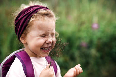 Portrait of small toddler girl outdoors in summer nature, tickling face with grass.の写真素材