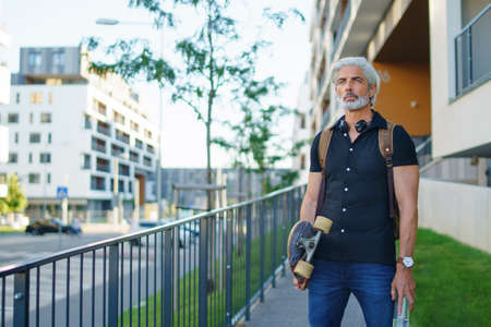 Portrait of mature man with skateboard outdoors in city, going back to work.の写真素材