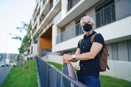 Mature man commuter with face mask and skateboard outdoors in city, coronavirus concept.の写真素材