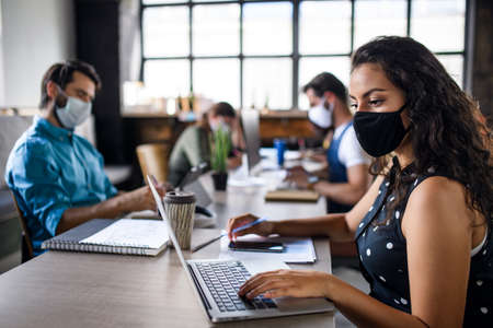 Business people with face masks indoors in office, back to work after coronavirus lockdown.の素材 [FY310155657040]