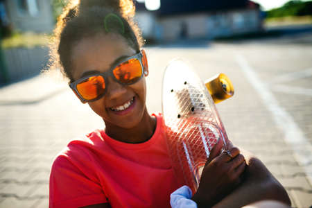 Front view of teenager girl with skateboard outdoors in city, looking at camera.の写真素材