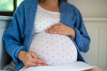 Unrecognizable pregnant woman sitting indoors at home.の写真素材