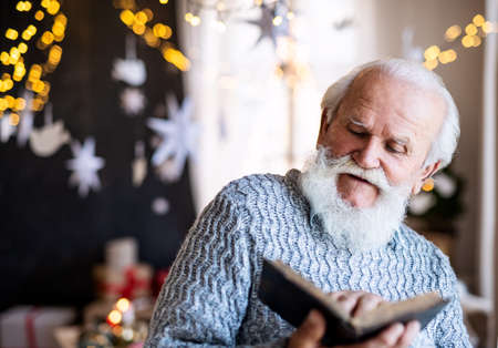 Front view of happy senior man indoors at home at Christmas, reading book.