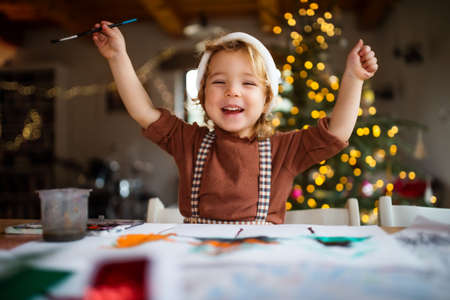 Portrait of small girl indoors at home at Christmas, painting pictures.の写真素材
