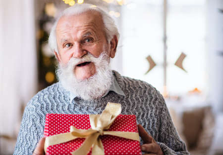 Front view of happy senior man with present box indoors at home at Christmas.の写真素材
