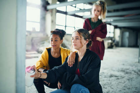 Group of teenagers girl gang indoors in abandoned building, using spray paint on wall.の写真素材