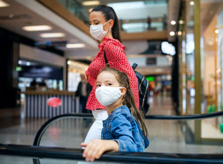 Mother and daughter with face mask on escalator indoors in shopping center, coronavirus concept.の写真素材
