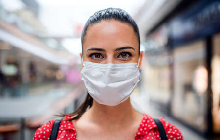 Woman with face mask standing indoors in shopping center, coronavirus concept.