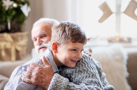 Small boy with senior grandfather indoors at home at Christmas, hugging.の写真素材