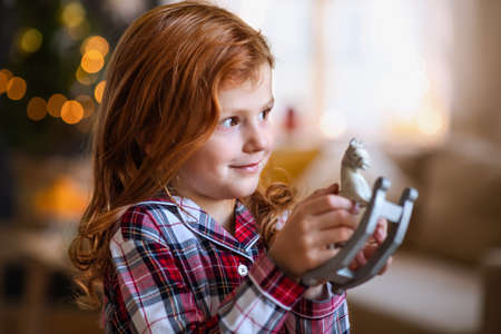 Portrait of small girl indoors at home at Christmas, holding wooden horse.の写真素材