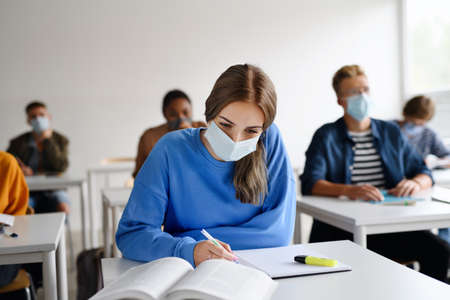 Young students with face masks at desks at college or university, coronavirus concept.