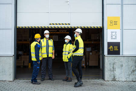 Group of workers with face mask talking in front of warehouse, coronavirus concept.の写真素材