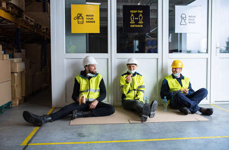 Group of workers eating snack indoors in warehouse, coronavirus concept.
