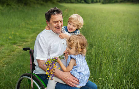 Small children with senior grandfather in wheelchair on a walk on meadow in nature.の写真素材