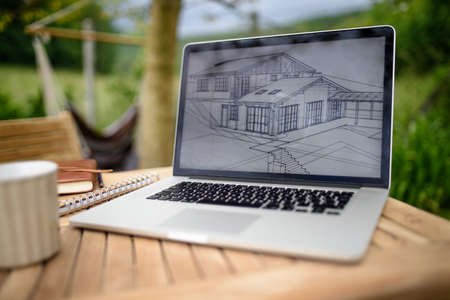 Laptop with blueprints on desk outdoors in garden, home office concept.の写真素材
