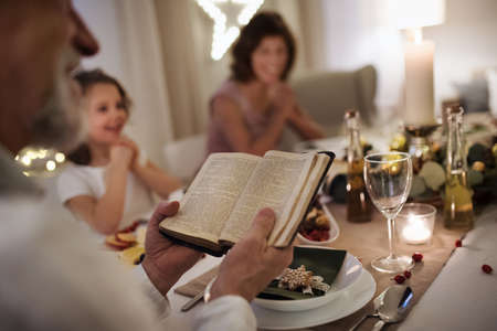 Small girl with grandparents sitting indoors celebrating Christmas together, bible reading.の写真素材