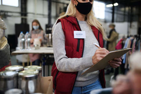 Volunteers working with food and clothes in community charity donations center, coronavirus concept.