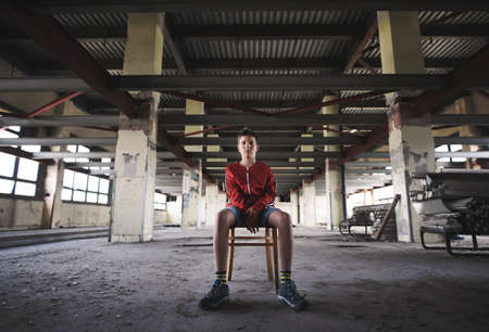 Sad and disappointed teenagers boy sitting indoors in abandoned building.