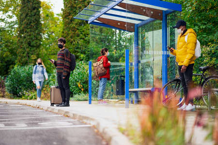 Young people with smartphones on bus stop outdoors in town. Coronavirus concept.