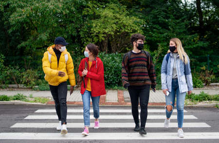 Group of young people crossing road outdoors in town, talking. Coronavirus concept.