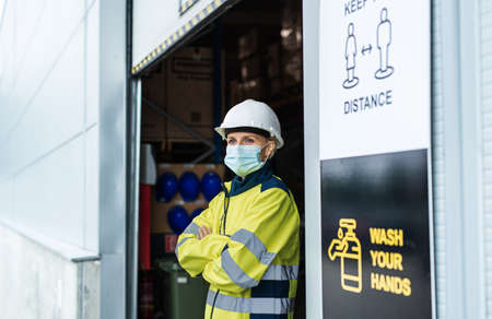 Woman worker with face mask standing in front of warehouse, coronavirus concept.