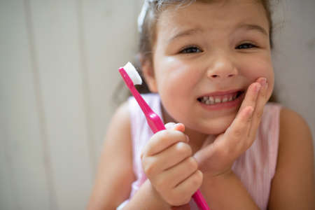 Front view portrait of worried small girl indoors, loosing baby tooth.