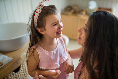 Crying small girl with mother indoors, loosing baby tooth.