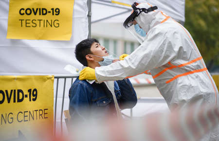 Young man in covid-19 testing center outdoors on street, coronavirus and taking swab concept.