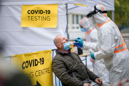 Senior man in covid-19 testing center outdoors on street, coronavirus and taking swab concept.