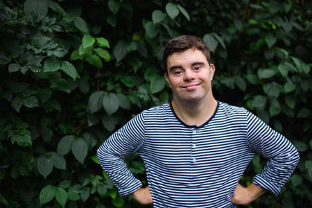 Portrait of down syndrome adult man standing outdoors at green background, looking at camera.
