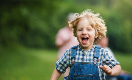Small boy with unrecognizable grandparents on a walk on meadow in nature, running.