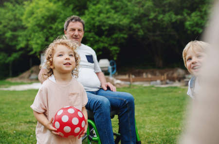 Small children with senior grandparents in wheelchair playing.