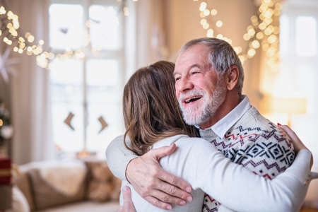 Senior man with young woman indoors at home at Christmas, hugging.の写真素材