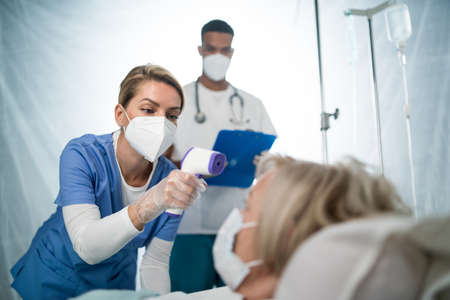 Doctors and covid-19 infected patient in bed in hospital, coronavirus and measuring temperature...