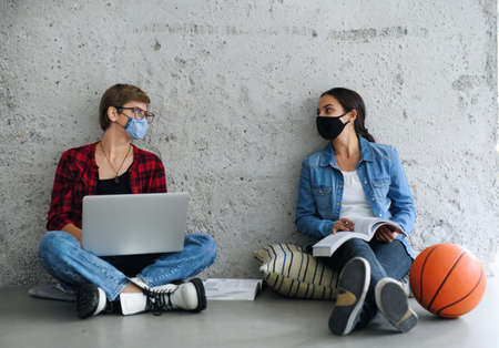 Young students with laptop sitting on floor back at college or university, coronavirus concept.の写真素材