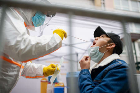 Young man in covid-19 testing center outdoors on street, coronavirus and taking swab concept.の写真素材