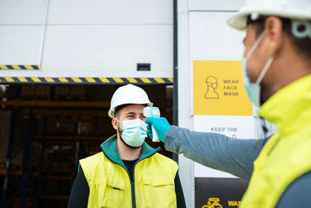 Workers with face mask in front of warehouse, coronavirus and temperature measuring concept.