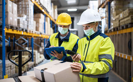 Workers with face mask working indoors in warehouse, coronavirus concept.
