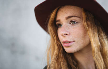 Portrait of young woman with red hair and hat standing against gray background.の写真素材