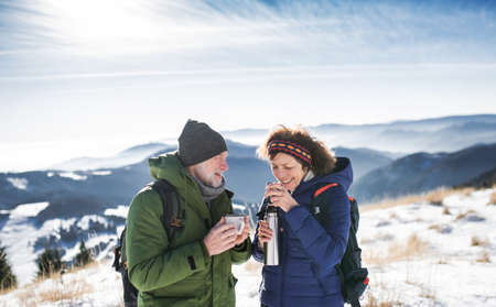 Senior couple hikers in snow-covered winter nature, drinking hot tea.