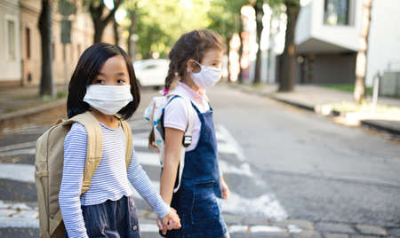 Small school girls with face mask outdoors in town, coronavirus concept.の写真素材