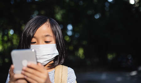 Small Japanese girl with smartphone outdoors in town, coronavirus concept.