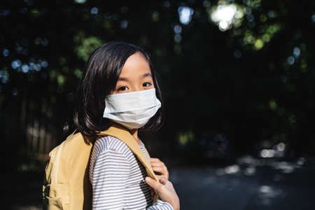 Portrait of small Japanese girl with backpack walking outdoors in town, coronavirus concept.