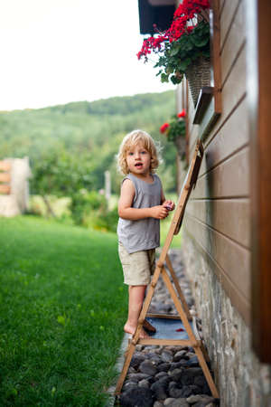 Happy small blond boy playing outdoors by house in summer.の写真素材